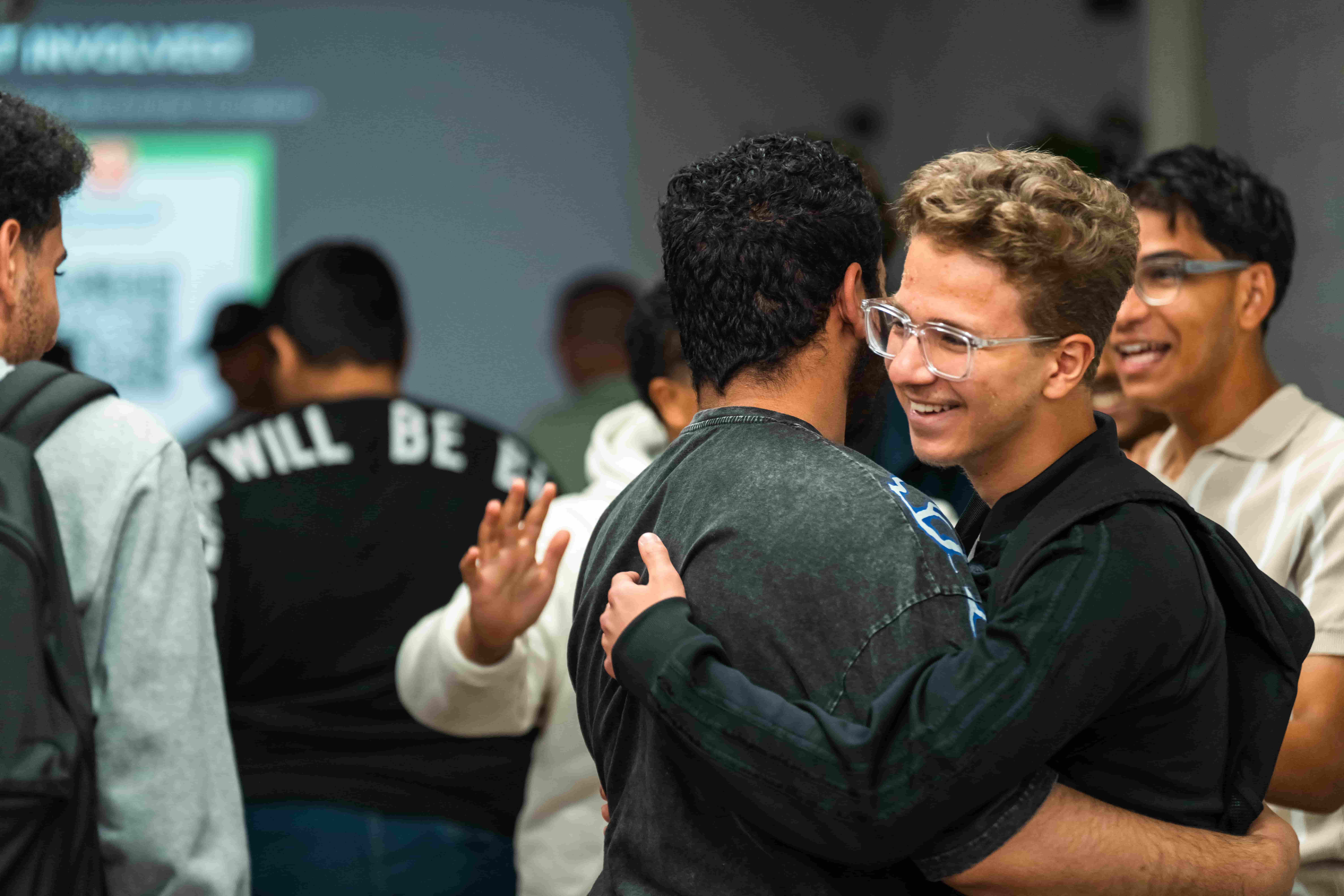Two young people embracing at a UMF session while others smile around them