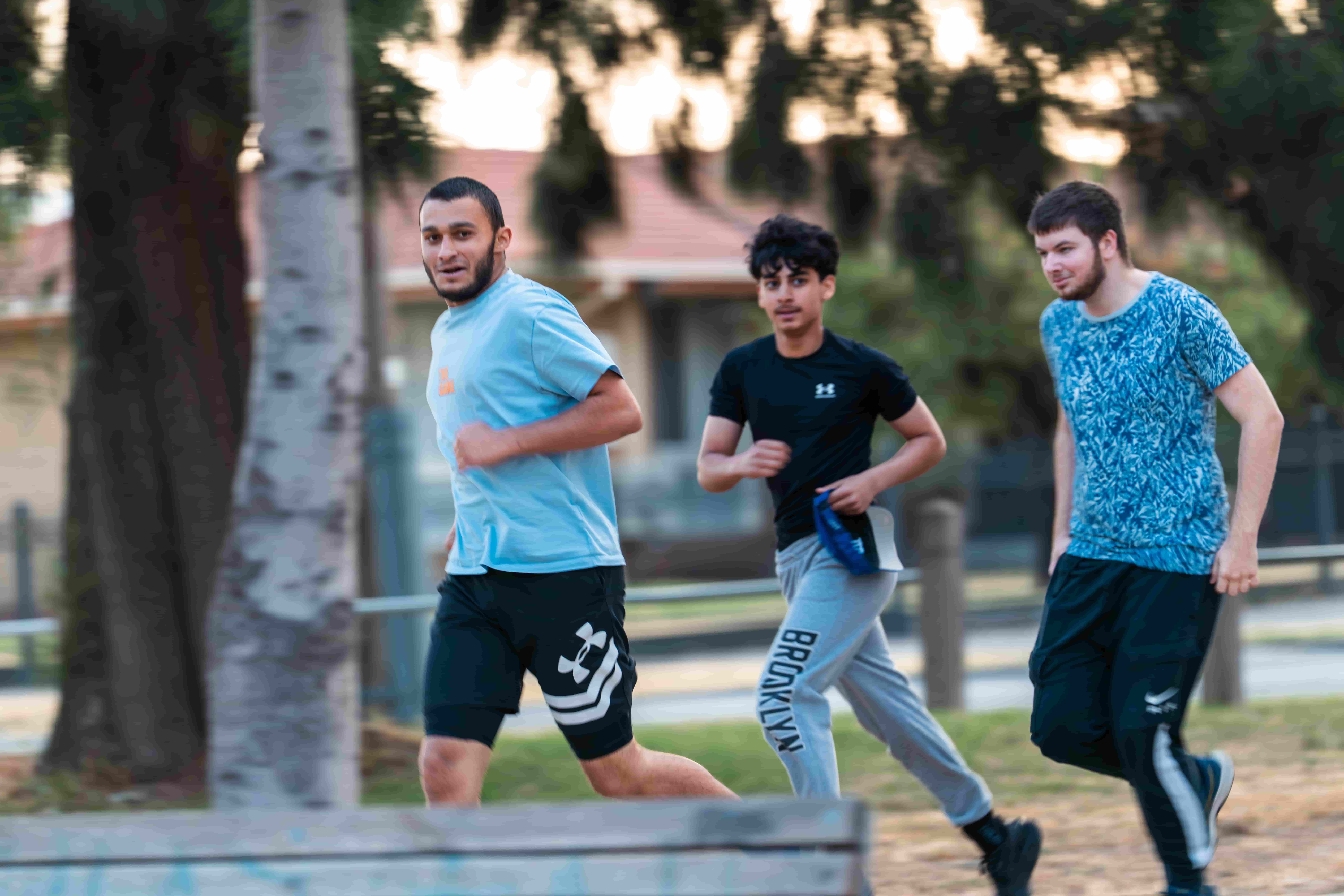 Three young men running together in a park at dusk during a UMF fitness session